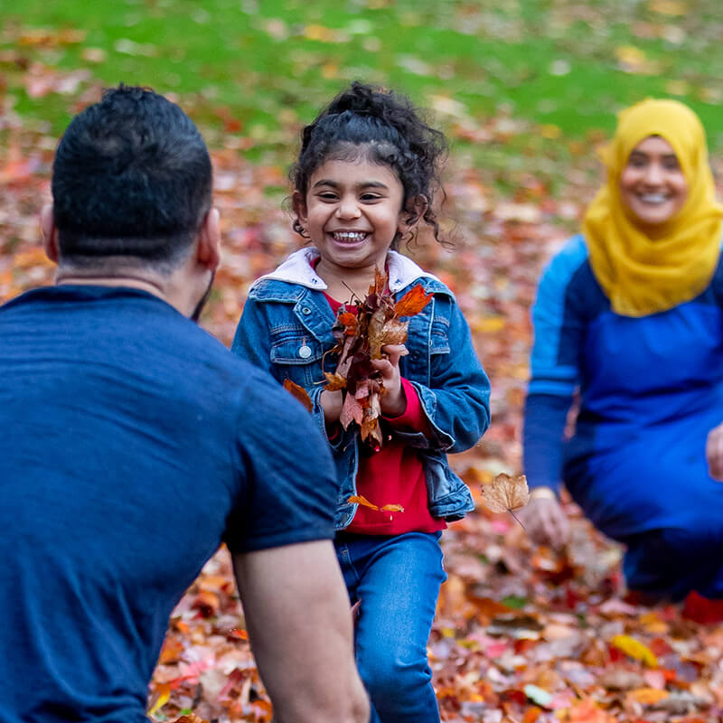 A young girl runs between her parents with a handful of autumn leaves