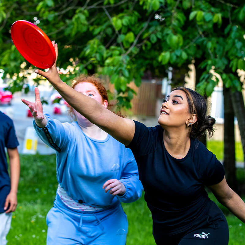 Two girls reach to grab a frisbee in a park